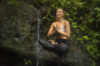 Açık havada genç güzel ve mutlu bir kadının portresi. Yoga ve meditasyon yapıyor. Tropikal yağmur ormanlarında lotus duruşunda oturuyor ve yaz tatillerinde doğanın tadını çıkarıyor.