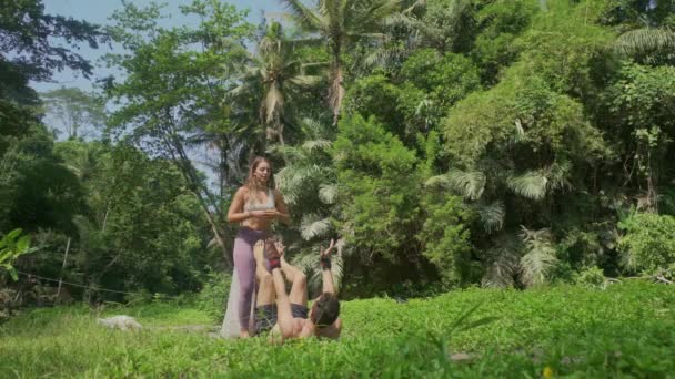 アクロヨガフライングウイングス運動 若い幸せと美しい女性ジャンプオン彼女のAcroyogaパートナーに熱帯緑の森で自由と健康的なライフスタイルのコンセプト — ストック動画