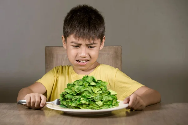 ほうれん草プレートの前のテーブルの上に座っているヒスパニックの子供を動揺させ うんざり新鮮な食べ物を拒否します子供の中でそれが嫌な緑の野菜の概念と健康的な栄養を見つける — ストック写真