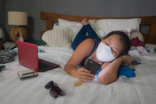 hand phone addiction in times of covid-19 - young bored and messy Asian Korean woman on chaotic bed using internet social media app as addict during coronavirus quarantine home lockdown