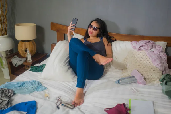 slackness and chaos at home lockdown - young disorderly and chaotic Asian Korean woman on bed taking selfie with mobile phone on grimy and messy bedroom in social media addiction