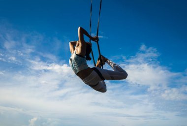 Genç, mutlu ve atletik Asyalı Endonezyalı bir kadının silüeti. Aero yoga antrenmanı yapıyor. Vücut dengesini dengede tutuyor.