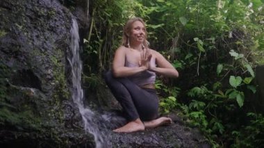 Açık havada genç güzel ve mutlu bir kadının portresi. Yoga ve meditasyon yapıyor. Tropikal yağmur ormanlarında lotus duruşunda oturuyor ve yaz tatillerinde doğanın tadını çıkarıyor.