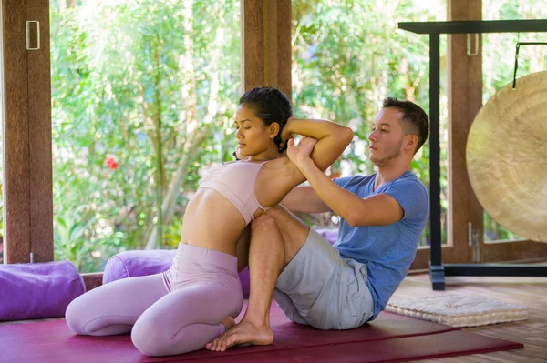 young attractive and fit masseur man giving traditional Thai massage to beautiful and relaxed Asian woman lying on studio ground receiving healing treatment at tropical spa