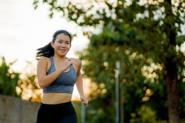 Açık hava koşusu antrenmanı - genç mutlu ve kendini işine adamış Asyalı kadın güzel şehir parkında ya da gün batımında kırsal yolda koşuyor sağlıklı yaşam tarzında spor ve kardiyo aktivitelerinin keyfini çıkarıyor