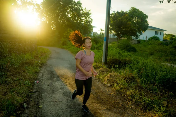 outdoors running workout - young happy and dedicated Asian Chinese woman jogging at beautiful city park or countryside trail on sunset enjoying fitness and cardio activity in healthy lifestyle