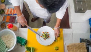 Asyalı profesyonel aşçının elleri restoran mutfağında lezzetli ve sağlıklı Japon suşi dürümleri hazırlıyor. Güzel malzemelerle geleneksel Japon yemekleri yapıyor.