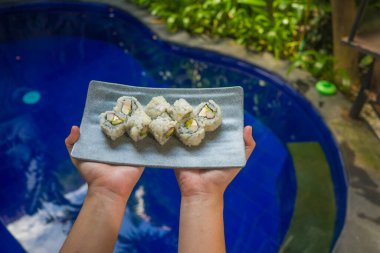 Japon gurme mutfağı. Geleneksel sağlıklı Asya yemekleri ve yaratıcı doğulu yemek kavramının gri sayfasında lezzetli ve lezzetli Japon suşi rulolarını sunan eller.