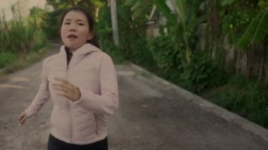 Açık havada idman - güzel şehir parkında ya da kırsal kesimde koşan sağlıklı yaşam tarzının tadını çıkaran genç mutlu ve kendini işine adamış Asyalı bir kadının görüntüsü.