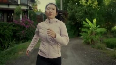 Açık havada idman - güzel şehir parkında ya da kırsal kesimde koşan sağlıklı yaşam tarzının tadını çıkaran genç mutlu ve kendini işine adamış Asyalı bir kadının görüntüsü.