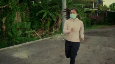 Kirlilik karşıtı yüz maskesi takan Asyalı bir kadın kendini adamış genç Çinli bir kızın üzerinde spor yapıyor gün batımında güzel şehir parkında koşuyor covid-19 pandemik zamanlarında spor yapıyor.