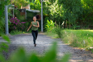 Açık havada idman - genç mutlu ve kendini Asya 'ya adamış Çinli kadın güzel şehir parkında ya da gün batımında kırsal yolda koşuyor sağlıklı yaşam tarzında spor ve kardiyo aktivitelerinin keyfini çıkarıyor.