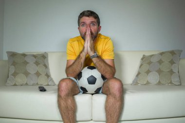 Genç heyecanlı ve gergin futbol taraftarı. Oturma odasındaki kanepede futbol maçı seyreden adam yoğun bir yüz ifadesi içinde duygu ve stres hissediyor.
