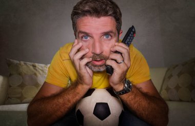 Oturma odasındaki kanepede futbol maçı izleyen heyecanlı ve gergin genç futbolcunun etkileyici portresi. Çılgınca bir duygu ve stres.