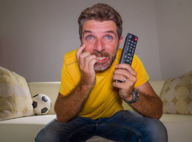 Oturma odasındaki kanepede futbol maçı izleyen heyecanlı ve gergin genç futbolcunun etkileyici portresi. Çılgınca bir duygu ve stres.