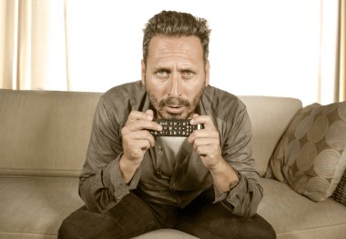 Oturma odasındaki kanepede oturup yoğun bir yüz ifadesiyle eğlenen ve televizyon haberleri ya da gerilim filmi izleyen genç ve odaklanmış adamın hayat tarzı portresi. 