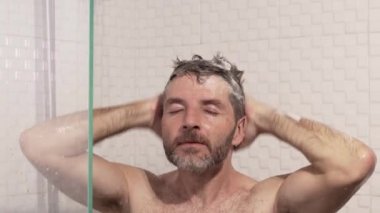 Sabah duşu. Sakallı, genç, çekici ve mutlu bir adamın evde duş alıp saçlarını şampuanla yıkarken sağlık ve hijyen kavramının keyfini çıkardığı bir fotoğraf.