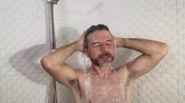 Sakallı, genç, çekici ve mutlu bir adam evde duş alıyor. Saçlarını şampuanla yıkıyor. Neşeli bir şekilde sabah duşunun tadını çıkarıyor.