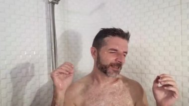 Sakallı, dans eden, duşta şarkı söyleyen kaygısız ve evde mikrofon tutuyormuş gibi yapan genç, çekici ve mutlu bir adamın komik bir fotoğrafı.