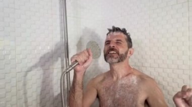 Sakallı, dans eden, duşta şarkı söyleyen kaygısız ve evde mikrofon tutuyormuş gibi yapan genç, çekici ve mutlu bir adamın komik bir fotoğrafı.