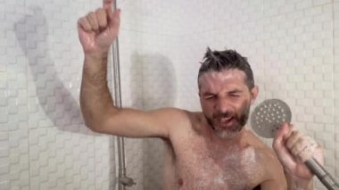 Sakallı, dans eden, duşta şarkı söyleyen kaygısız ve evde mikrofon tutuyormuş gibi yapan genç, çekici ve mutlu bir adamın komik bir fotoğrafı.