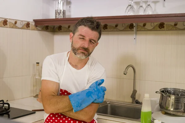 domestic chores stress - lifestyle portrait of young attractive overworked and stressed home cook man in red apron hating dishwashing feeling upset and unhappy washing dishes frustrated