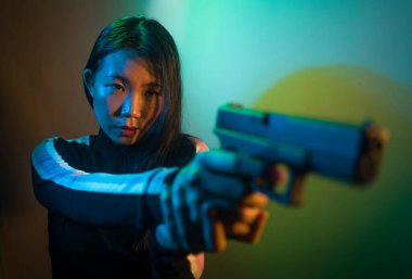 Çekici ve tehlikeli bir kadın ajanın ya da elinde tabanca olan Asyalı bir gangsterin, Hollywood film tarzında ateşli bir şekilde silahını doğrultmuş sinemalı bir portresi.