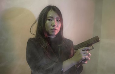 Çekici ve tehlikeli kadın ajanın sinematik portresi. Casus ajan ya da elinde silah tutan Asyalı Koreli gangster kız. Hollywood film tarzında ateşli bir şekilde silahı doğrultuyor.