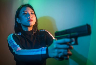 Çekici ve tehlikeli kadın ajanın sinematik portresi. Casus ajan ya da elinde silah tutan Asyalı Koreli gangster kız. Hollywood film tarzında ateşli bir şekilde silahı doğrultuyor.