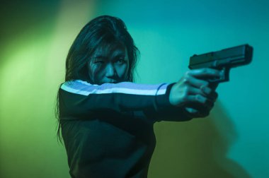 Çekici ve tehlikeli kadın ajanın sinematik portresi. Casus ajan ya da elinde silah tutan Asyalı Koreli gangster kız. Hollywood film tarzında ateşli bir şekilde silahı doğrultuyor.