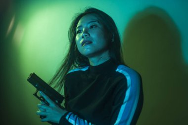 Çekici ve tehlikeli kadın ajanın sinematik portresi. Casus ajan ya da elinde silah tutan Asyalı Koreli gangster kız. Hollywood film tarzında ateşli bir şekilde silahı doğrultuyor.