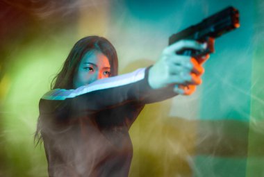 Çekici ve tehlikeli kadın ajanın sinematik portresi. Casus ajan ya da elinde silah tutan Asyalı Koreli gangster kız. Hollywood film tarzında ateşli bir şekilde silahı doğrultuyor.
