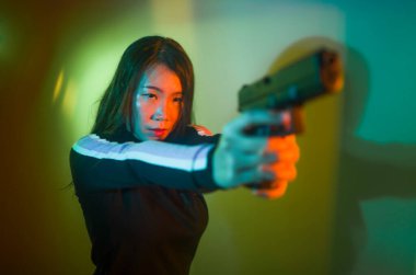 Çekici ve tehlikeli kadın ajanın sinematik portresi. Casus ajan ya da elinde silah tutan Asyalı Koreli gangster kız. Hollywood film tarzında ateşli bir şekilde silahı doğrultuyor.