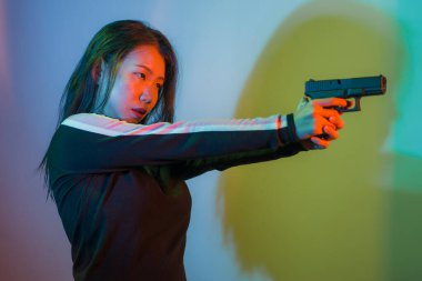 Çekici ve tehlikeli kadın ajanın sinematik portresi. Casus ajan ya da elinde silah tutan Asyalı Koreli gangster kız. Hollywood film tarzında ateşli bir şekilde silahı doğrultuyor.