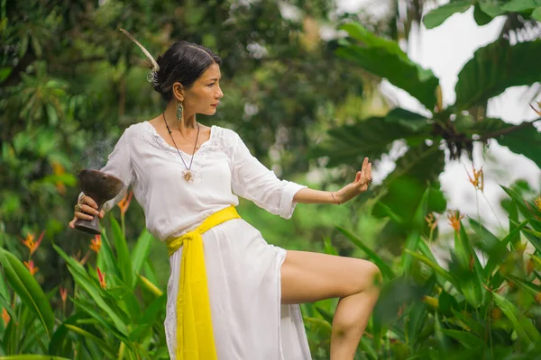 mind and body connection - beautiful and happy healer Asian woman holding incense cup doing ritual traditional healing dance at green tropical forest in wellness and healthy lifestyle