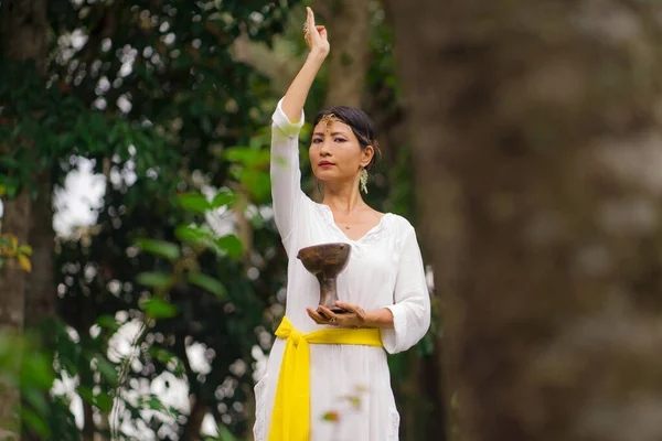 mind and body connection - beautiful and happy healer Asian woman holding incense cup doing ritual traditional healing dance at green tropical forest in wellness and healthy lifestyle