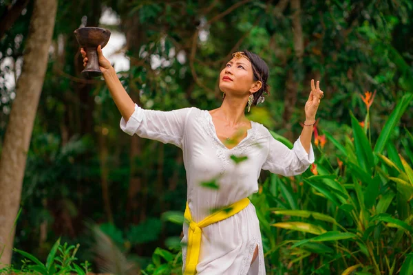 mind and body connection - beautiful and happy healer Asian woman holding incense cup doing ritual traditional healing dance at green tropical forest in wellness and healthy lifestyle