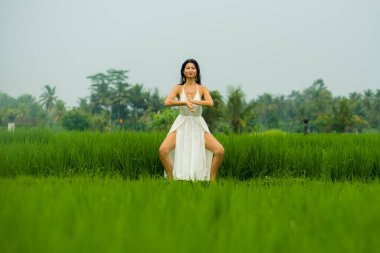 Doğa ile beden ve zihin bağlantısı - Mutlu ve güzel Asyalı Koreli kadın dışarıda yoga yapıyor ve meditasyon yapıyor. Cennet yeşil pirinç tarlasında tropikal yaz tatillerinin tadını çıkarıyor.