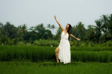 Doğa ile zihin ve beden bağlantısı - Orta yaşlı, çekici ve mutlu, yaz elbiseli Asyalı kadın, tropikal varış noktasında dans ediyor.