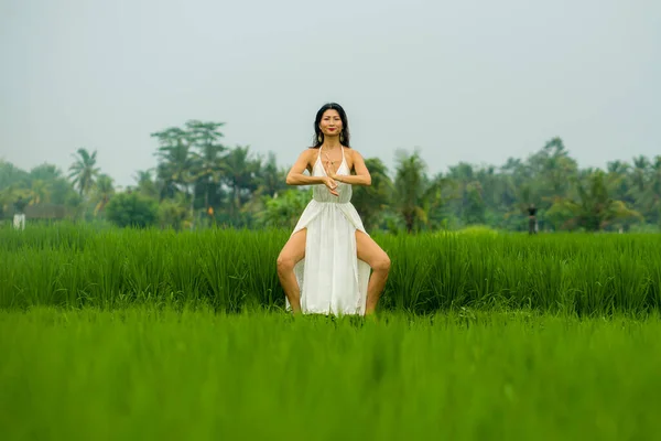 body and mind connection with nature - happy and beautiful Asian Korean woman doing yoga and meditation exercise outdoors at idyllic green rice field enjoying tropical Summer holidays