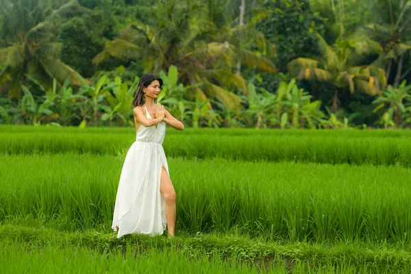 body and mind connection with nature - happy and beautiful Asian Korean woman doing yoga and meditation exercise outdoors at idyllic green rice field enjoying tropical Summer holidays