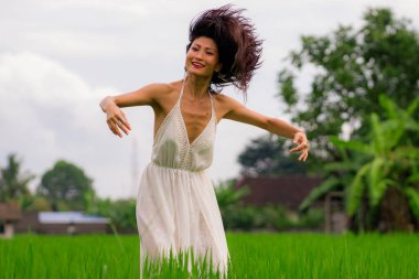 Açık havada tatil portresi. Çekici ve mutlu orta yaşlı Asyalı beyaz elbiseli kadın. Yeşil alan manzarasında özgürlük ve doğanın tadını çıkartıyor.