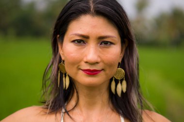 Açık havada tatil portresi. Çekici ve mutlu orta yaşlı Asyalı beyaz elbiseli kadının yeşil alan manzarasında özgürlük ve doğanın tadını çıkarırken tasasız ve neşeli.