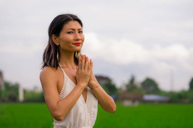 Açık havada tatil portresi. Çekici ve mutlu orta yaşlı Asyalı beyaz elbiseli kadının yeşil alan manzarasında özgürlük ve doğanın tadını çıkarırken tasasız ve neşeli.