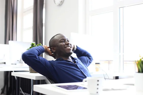 Relajado hombre de negocios afroamericano sentado en su escritorio mirando al aire. —  Fotos de Stock