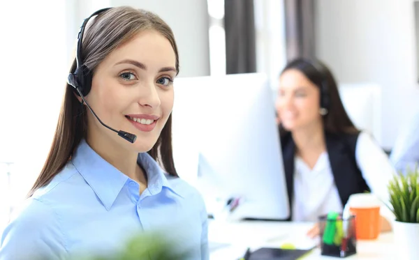 Glimlachende vrouwelijke call center operator doet haar werk met een headset terwijl ze naar de camera kijkt. — Stockfoto