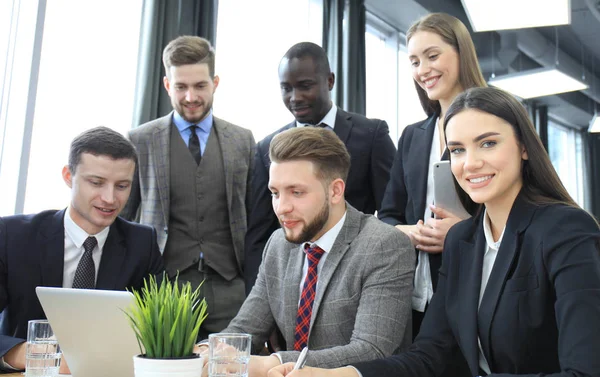 Brainstorming. Un gruppo di uomini d'affari che guardano insieme il portatile. Una donna d'affari guardando la macchina fotografica . — Foto Stock