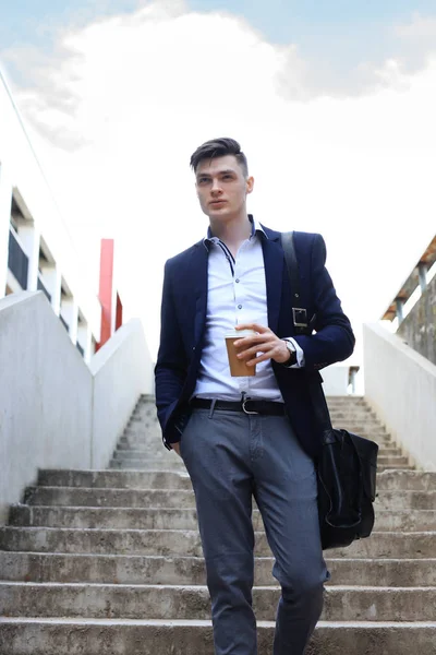 Um belo jovem empresário caminhando para o trabalho com sua pasta e um café . — Fotografia de Stock