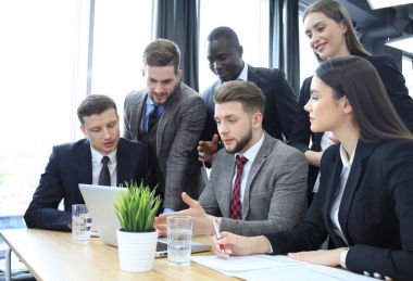 Girişim ekibi, modern parlak ofis içinde toplantı ve dizüstü bilgisayar üzerine çalışıyor.