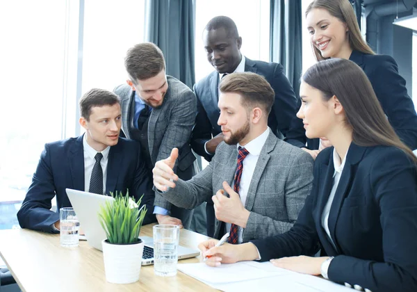 Brainstorming. Un gruppo di uomini d'affari che guardano insieme il portatile. Una donna d'affari guardando la macchina fotografica . — Foto Stock